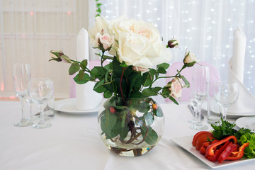 White roses in a vase on a decorated food table. Making a Banquet table with flowers and dishes. Festive table decorated with white roses.