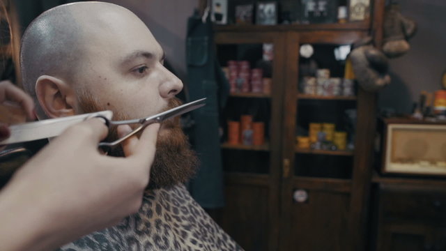 Barber woman trimming mustach of client with scissors at barbershop, slow motion