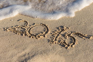 Inscription 2015 on sandy beach with wave's foam