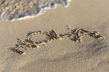 Inscription Hola on sandy beach with wave's foam