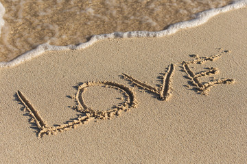 Inscription Love on sandy beach with wave's foam