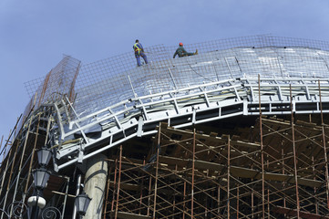 Construction workers-roofers, tied with ropes for protection work on the roof of a new building -...