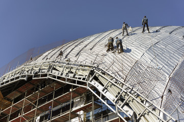 Construction workers-roofers, tied with ropes for protection work on the roof of a new building - the dome of the new building of the Philharmonic Orchestra in Skopje - Macedonia under construction 1