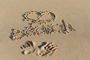Inscription Beach and handprints on sand