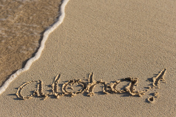 Inscription Aloha on sandy beach with wave's foam