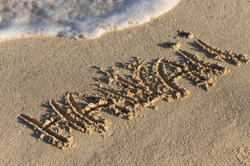 Inscription Hawaii on sandy beach with wave's foam