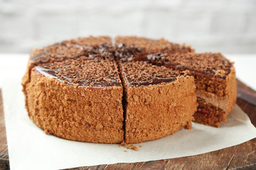 Sliced chocolate cake on wooden table, on light background