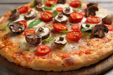 Tasty fresh pizza decorated with mushrooms and tomatoes on wooden background, close up