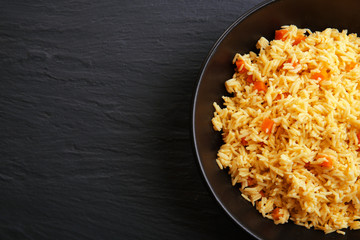 Stewed rice with a carrot on a plate over black background, close up
