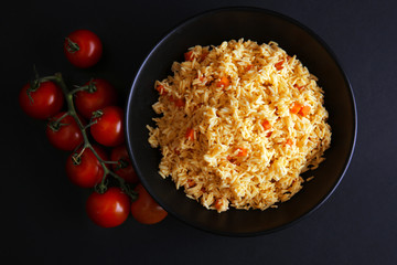 Stewed rice with a carrot and tomatoes on a plate over black background, close up