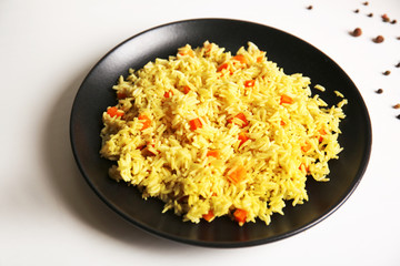 Stewed rice with a carrot on a black plate, close up