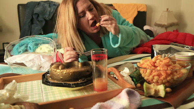 Portrait of a woman in depression lying on a bed and eating junk food