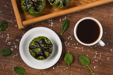 Fresh muffins with spinach, desiccated coconut, chocolate glaze and cup of coffee, delicious healthy dessert