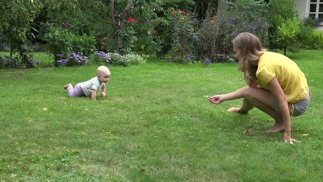 little baby girl crowl on grass to mother with pacifier in hand. Leisure, freetime and game with baby in garden. 4K UHD video clip.
