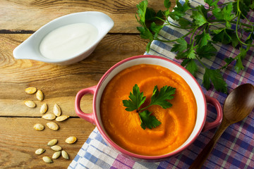 Autumnal spicy roasted pumpkin squash cream soup with parsley in the purple-pink soup bowl on the dark wooden background with checkered linen napkin, top view 