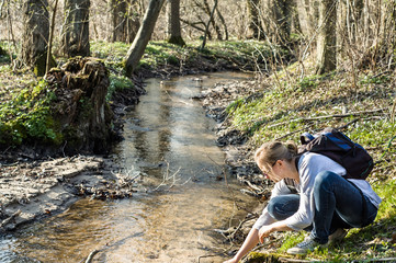 Hiking and relaxation. Young woman hiker with backpack by the river in the spring forest.