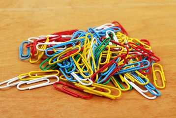 Hill of multicolored paper clips on a wooden board