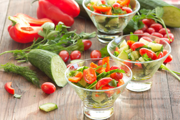 Three glass bowls with a salad of fresh vegetables and ingredients - tomato, cucumber, bell pepper on a dark wooden background
