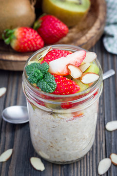 Overnight oatmeal with fresh strawberry and kiwi, garnished with sliced almond in  glass jar