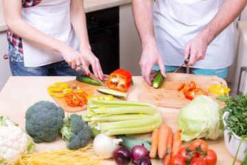 man and woman cooking together raw vegetables