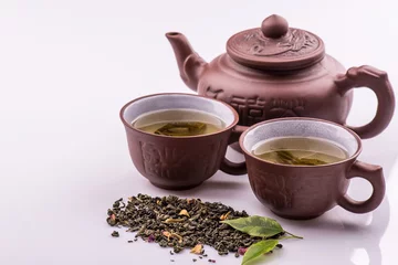 Foto op Aluminium Green tea in a cup and teapot, petals of green tea on a bamboo mat on a white background © nataliiaGL