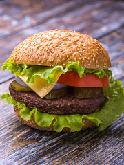 Hamburger with beef cutlet, fresh vegetables: tomatoes, onions, lettuce, sauce and bun with sesame seeds on a wooden background