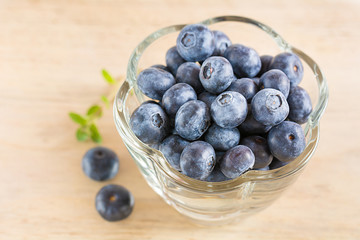 Frische Heidelbeeren in einer Glasschale stehen auf einem Holzbrett