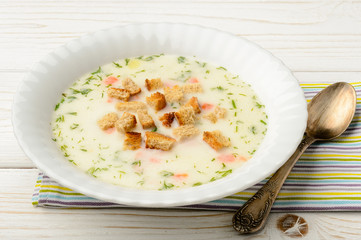Cheese soup in white bowl on white wooden table.