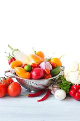 Fresh vegetables in metal colander over white.