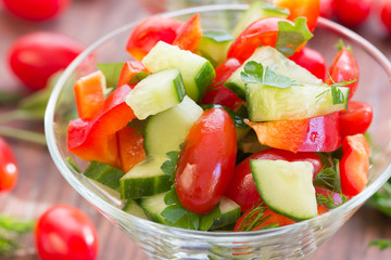 glass bowl with a salad of fresh vegetables and ingredients - tomato, cucumber, bell pepper on a dark wooden background
