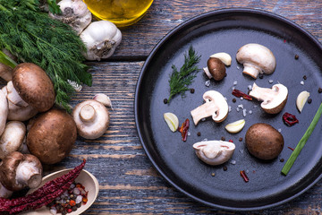 Mushrooms, parsley, dill, onion, olive oil, spices - ingredients for the preparation of mushroom dishes in a frying pan on a wooden background