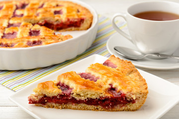 Piece of cherry pie and cup of tea on wooden table.