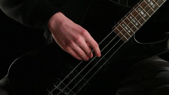man playing bass guitar at black background
