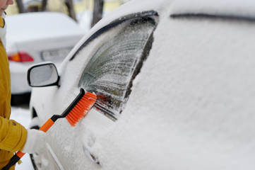 A woman in winter removes snow with the car.