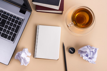 Office table desk with supplies, white blank note pad, cup, pen, pc, crumpled paper, flower on wooden background. Top view