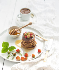 Breakfast set. Buckwheat pancakes with fresh garden strawberries, honey and cup of coffee over white wooden background