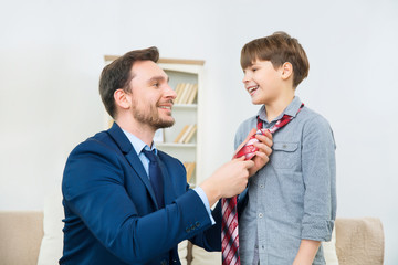 Young businessman helping smiling son to knot tie