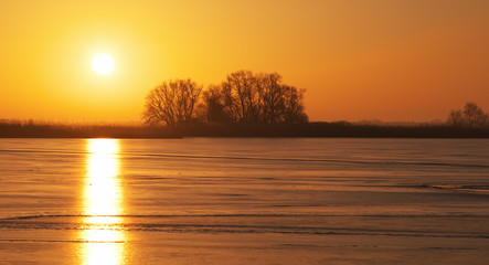 Winter landscape with frozen lake and sunset fiery sky.