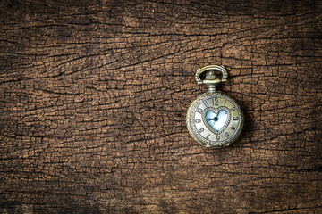 Small vintage brass clock with heart shape. Wooden background.