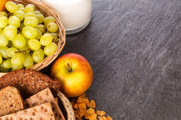 Frühstückszutaten Obst, Brot, Milch, Getreideflocken auf Granitplatte