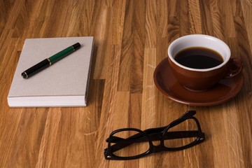 Nerdbrille mit Notizbuch und Kaffeetasse auf Holtztisch