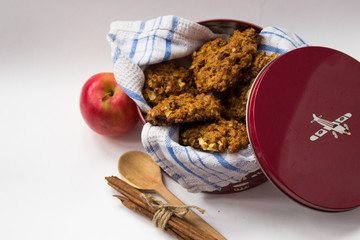 Several homemade oatmeal cookies in a red metal box with plane on it. Apple, cinnamon sticks, White background. Isolated
