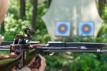 Man aiming crossbow at targets in summer forest