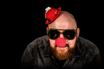 Man with beard wearing red nose, sunglasses and funny hat