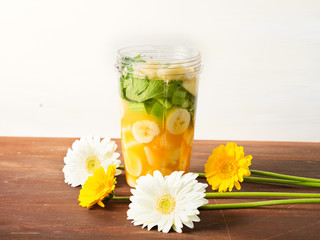Mixer glass with fruit and vegetables for a smoothie (banana, orange juice, pear, ginger and celery) with spring color flowers around on brown wooden table, copy space