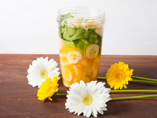 Mixer glass with fruit and vegetables for a smoothie (banana, orange juice, pear, ginger and celery) with spring color flowers around on brown wooden table