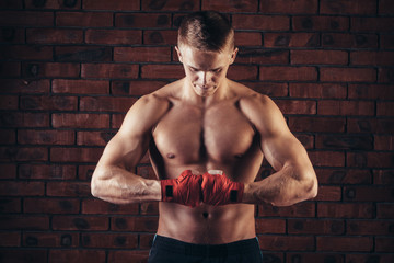 Fototapeta premium Muscular Fighter With Red Bandages against the background of a brick wall