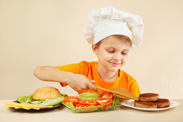 Little boy in chef hat puts meat on the hamburger