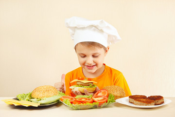 Little funny chef in chefs hat preparing a hamburger