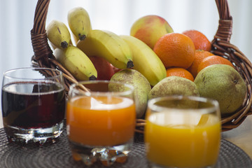 Multi fruit citrus juice from oranges, lemons, bananas, grapes in a glass with fruit basket in the background